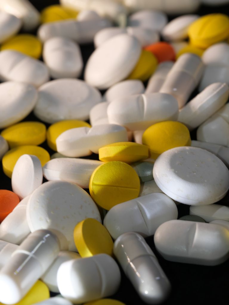 A close-up of various colored capsules and pills scattered on a black surface.